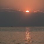 Captivating sunrise over calm ocean waters creates a tranquil scene with reflection and soft hues.